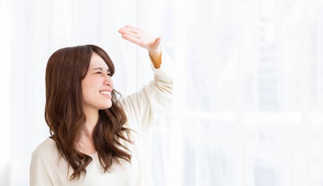 窓から入りこむ太陽の光がまぶしく、手で目を隠している女の人